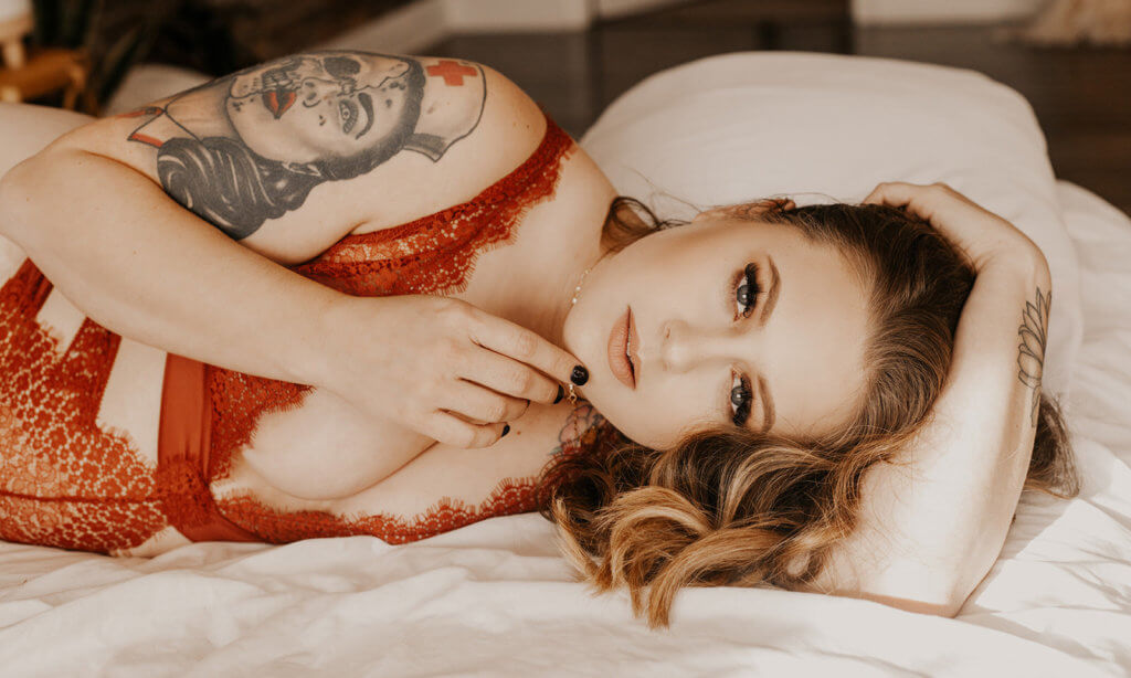 Kobieta z tatuażem na ramieniu, w czerwonej bieliźnie leżąca na łóżku 