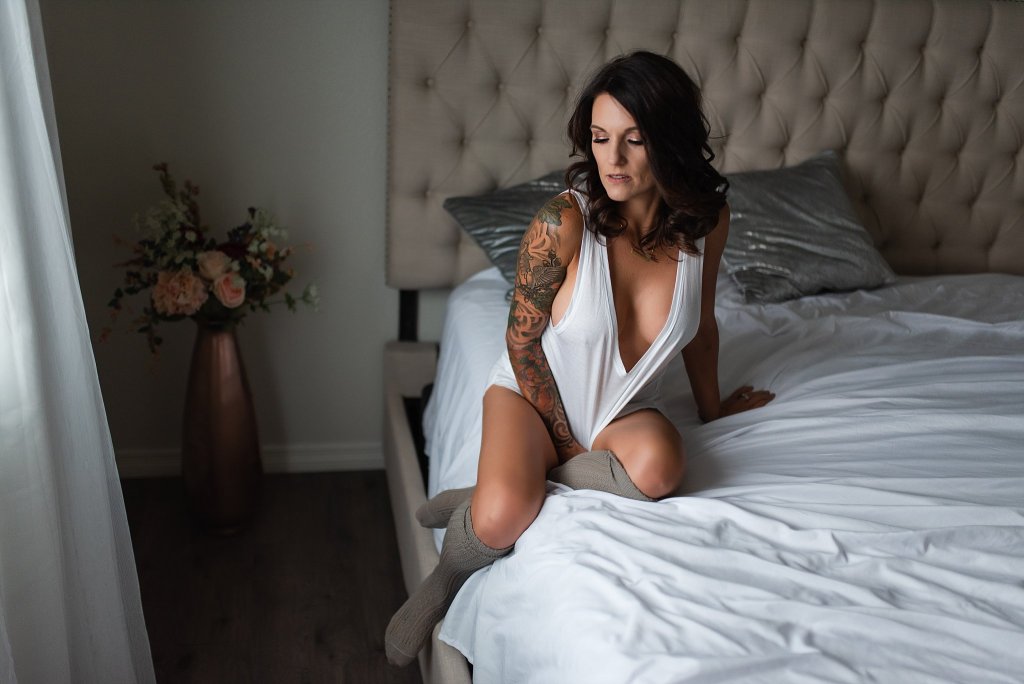 Kobieta z tatuażami na ręce w białej koszulce siedząca na łóżku 