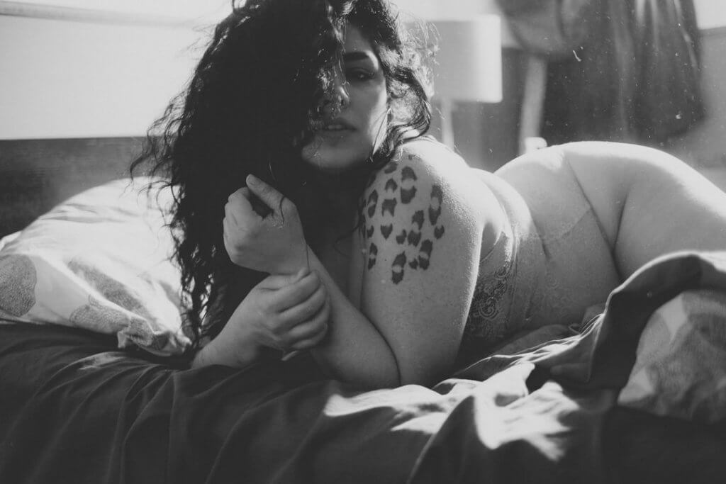Kobieta z tatuażem na ramieniu, leżąca w bieliźnie na łóżku 