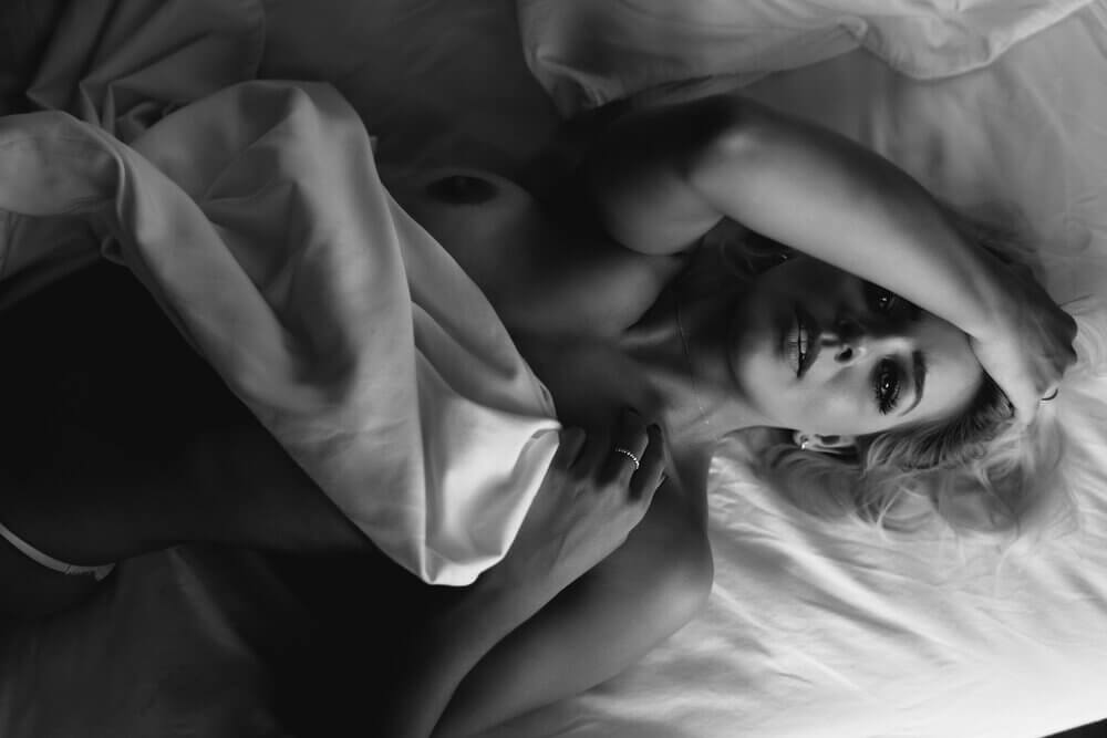 Naga kobieta leżąca na łóżku, trzymająca się z głowę